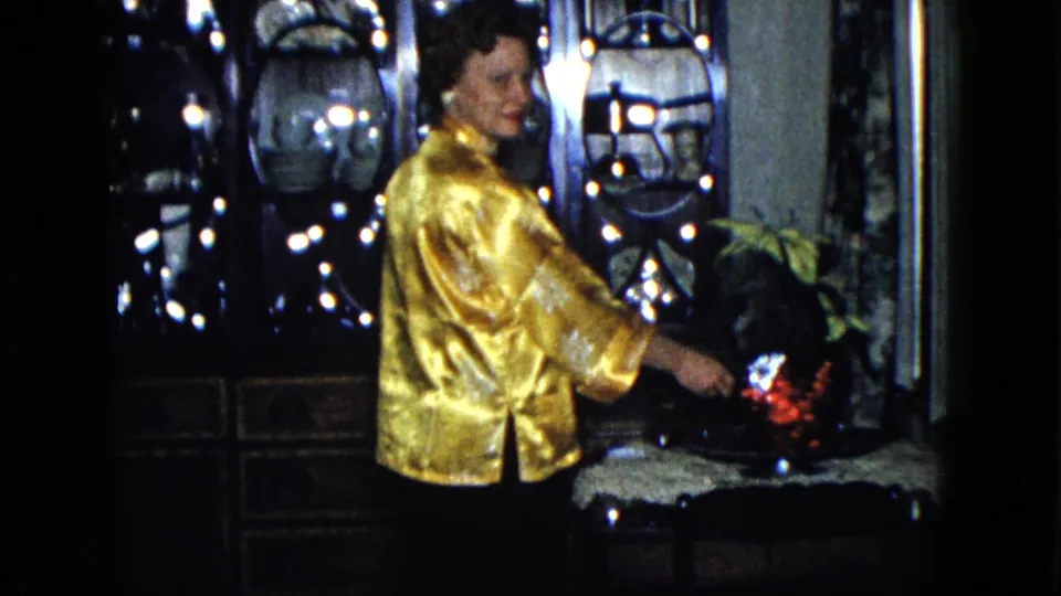 A woman in a gold satin robe reaches toward a glowing red-lit area in a dim 1958 Las Vegas interior.