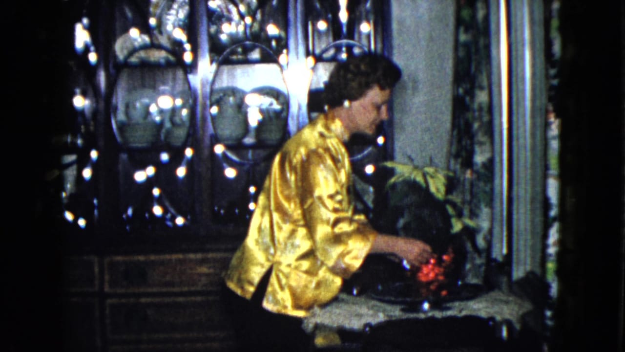 Woman bends toward a vase of red flowers on a table in a dim room.