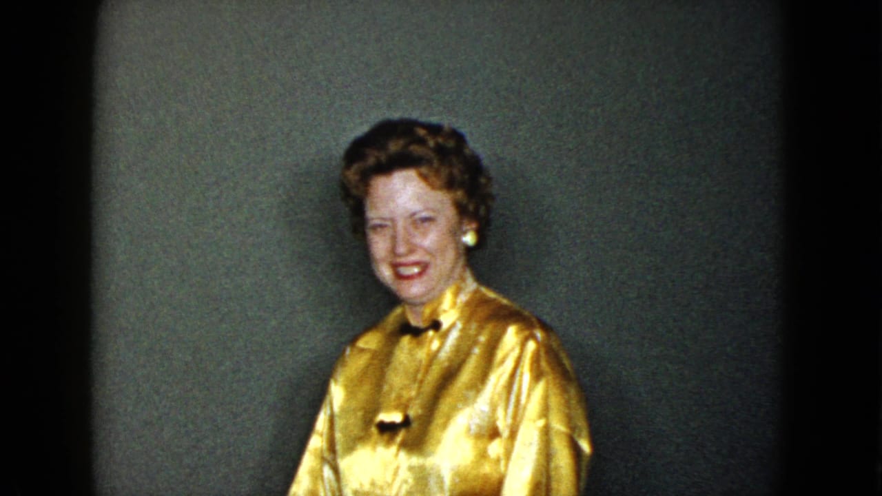 In 1958 Las Vegas home-movie footage, a well-dressed woman in a gold blouse smiles inside a private room.