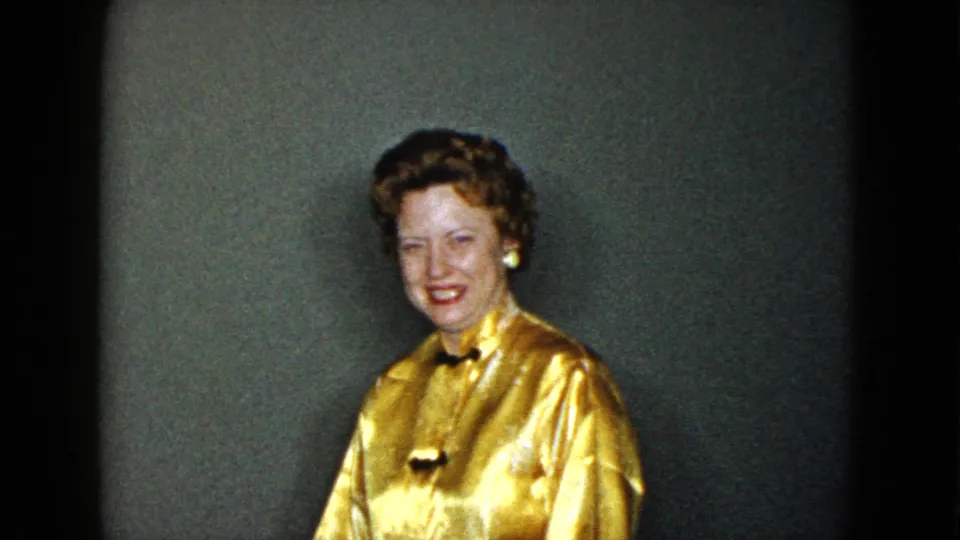 In 1958 Las Vegas home-movie footage, a well-dressed woman in a gold blouse smiles inside a private room.