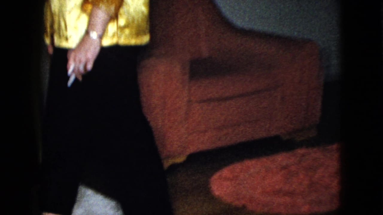 Woman's torso and hand holding a cigarette beside a red chair.