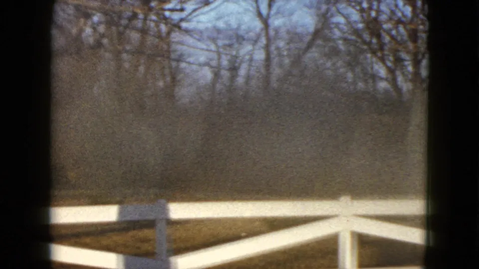 1958 Las Vegas home-movie frame showing a white ranch-style fence, open yard, and leafless trees beyond the enclosure.