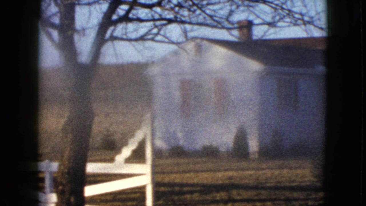 1958 8mm frame of a white farmhouse with red shutters behind a white fence, seen through bare trees in the Las Vegas metadata context.
