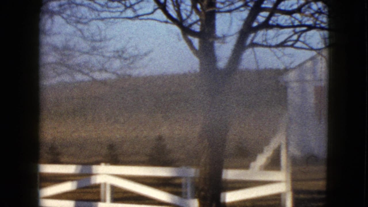 The pan shifts across a white fence and leafless tree, with the farmhouse partly visible in soft 8mm focus.