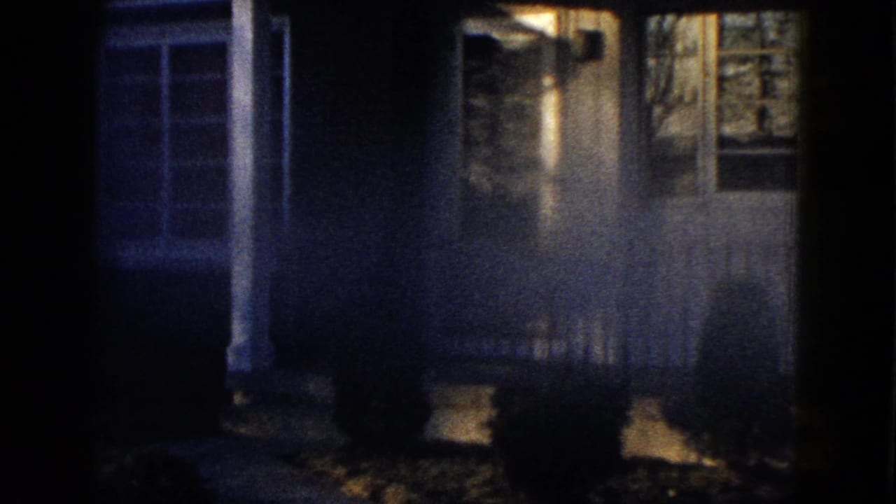 1958 Las Vegas home-movie frame showing a dim residential facade, porch posts, windows, shrubs, and front yard.