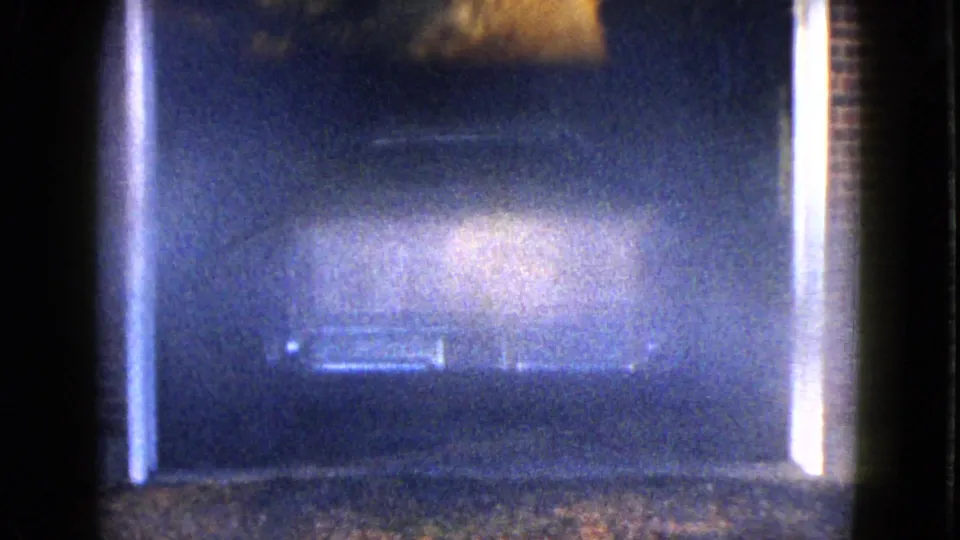 1958 Las Vegas-area 8mm frame with blue-black darkness, bright gate-edge flare, and a faint pale blur near center.