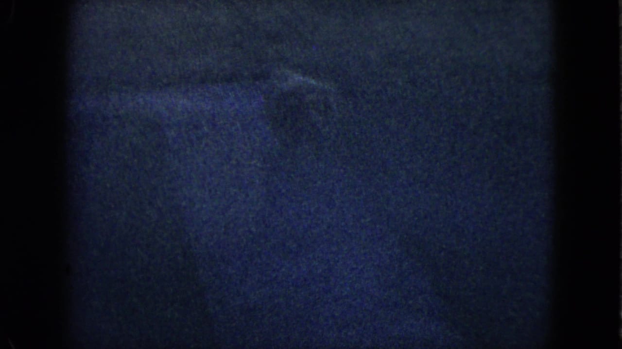 Dark grainy frame with indistinct blue-black shapes and film gate edges.