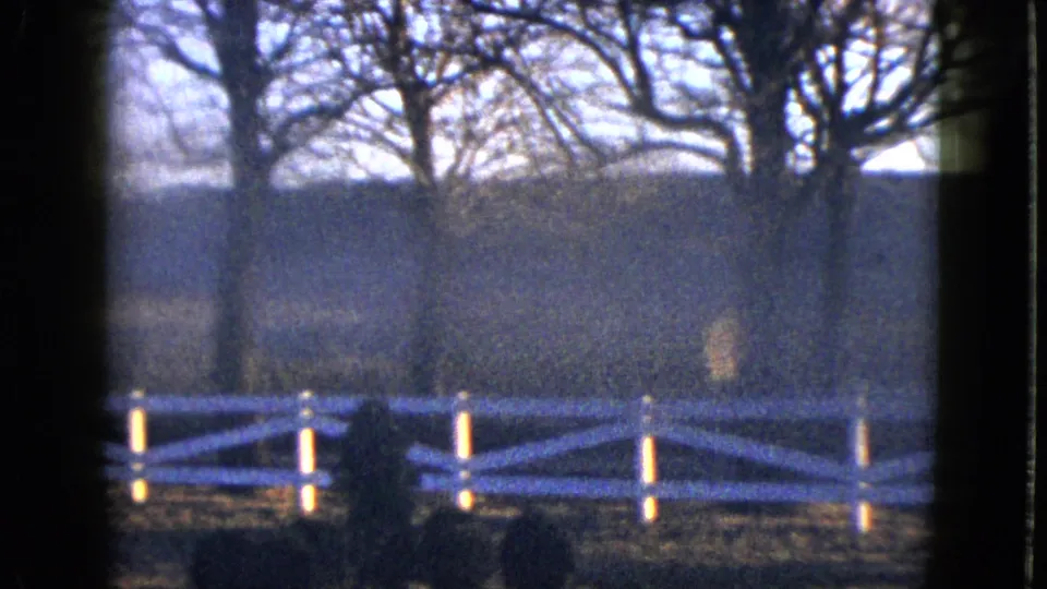 1958 Las Vegas-area 8mm frame looking through a dark window edge toward a white fence, bare trees, and hillside.