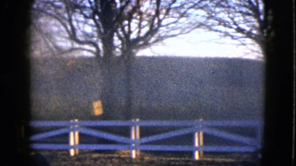 1958 Las Vegas-area 8mm view of a white fence, bare trees, hillside, and warm sunlit patch through a window-like frame.