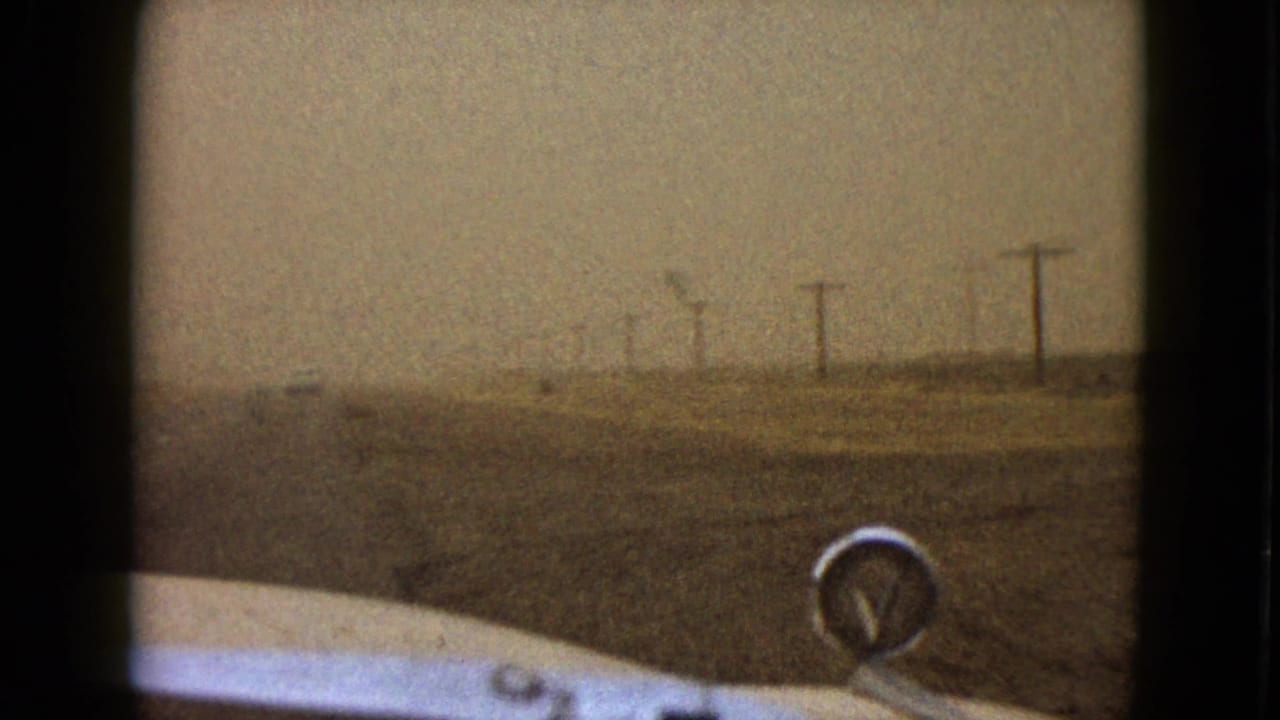 1958 Las Vegas-area 8mm frame looking over a vintage car hood toward a hazy road and utility poles.
