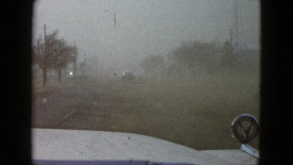 1958 8mm windshield view in the Las Vegas area, showing haze, roadside trees, and distant traffic lights.