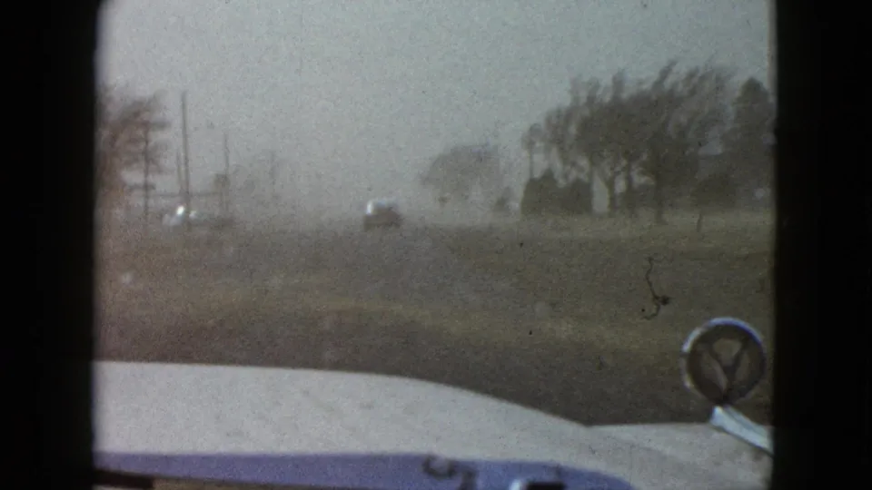 Las Vegas-area 1958 home-movie frame of a car moving through dusty haze past trees and utility poles.