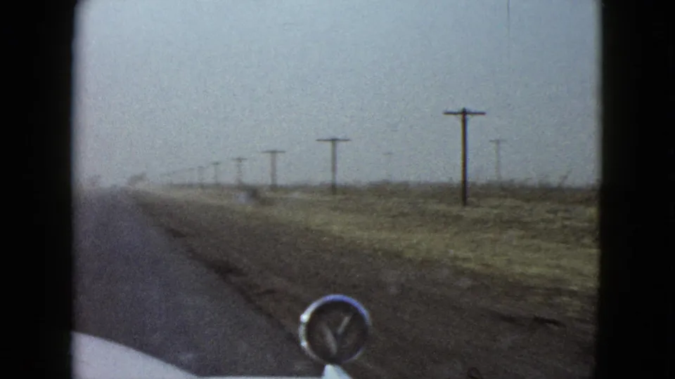 Final 1958 Las Vegas-area frame shows the car moving along a sparse desert road with telephone poles, brush, and a hazy sky ahead.