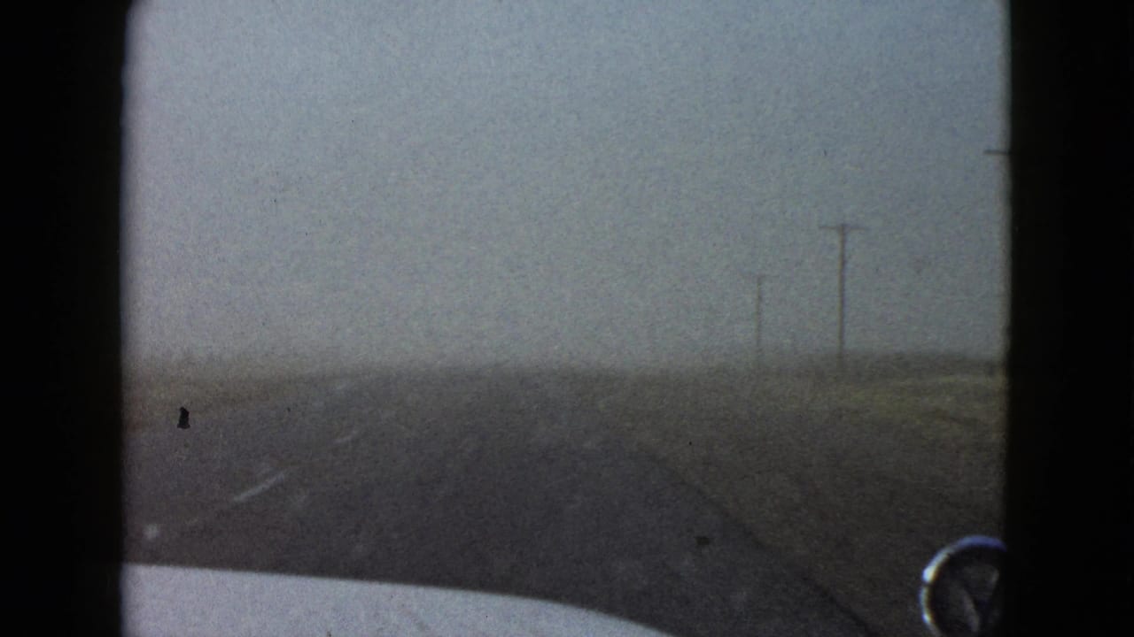 In-car 8mm view of a desolate roadway near Las Vegas in 1958, with telephone poles fading into haze.