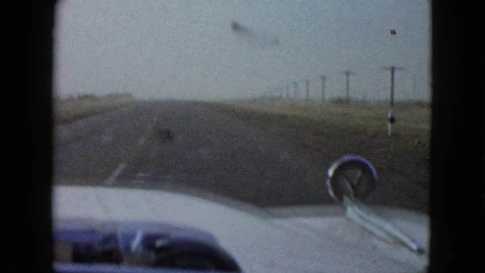 Windshield perspective from a 1958 road trip near Las Vegas, with the car hood foregrounding a straight rural highway.