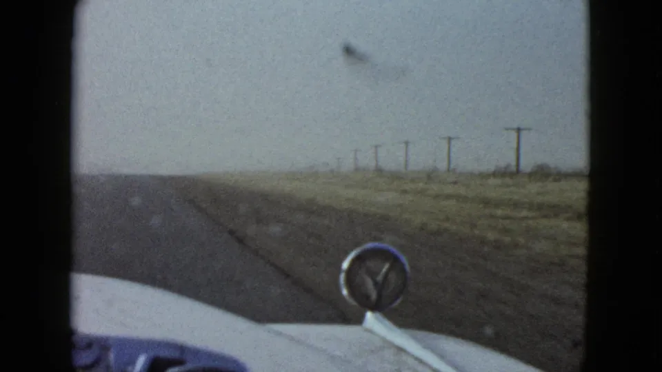 1958 Las Vegas-area 8mm frame showing an in-car view of a sparse road, dry ground, and roadside utility poles.