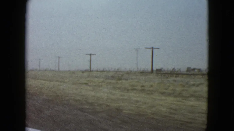 Open Las Vegas-area roadside seen from a moving car, with sparse scrubland, utility poles, and a soft hazy sky.