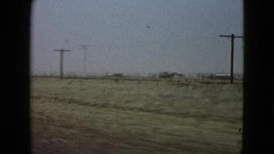 A moving-car view across low roadside vegetation and utility poles in the Las Vegas-area landscape described by the clip metadata.