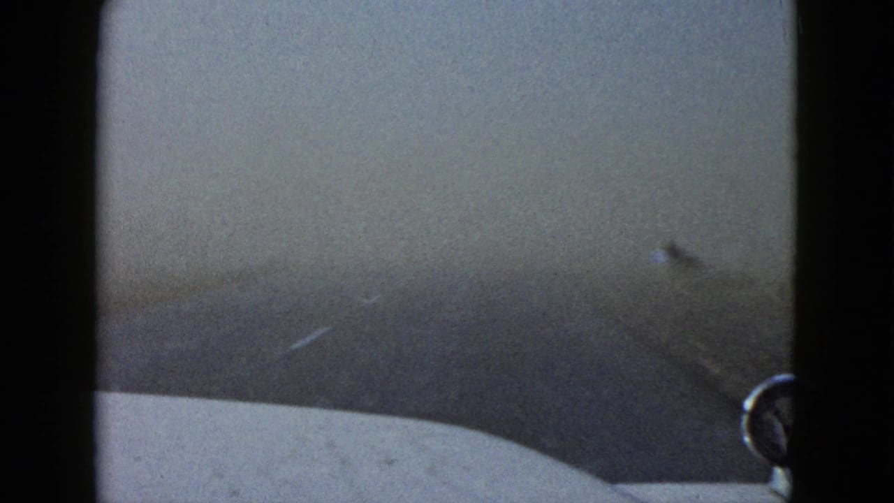 Dense fog obscures the road ahead in this 1958 Las Vegas-area driving view, with the car hood and roadside shape barely visible.