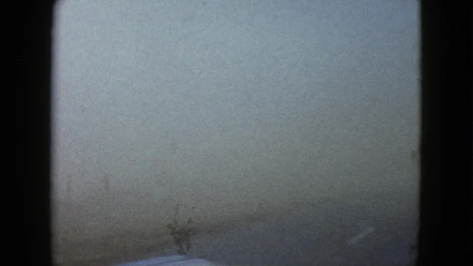 Fog thickens across the windshield view, leaving only a faint road surface and the car hood visible in the 1958 home-movie frame.