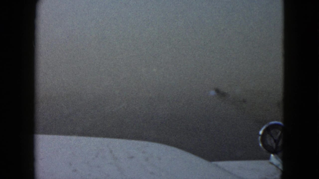 Fog begins to thin in this 1958 Las Vegas driving view, revealing the car hood edge and a round foreground emblem.