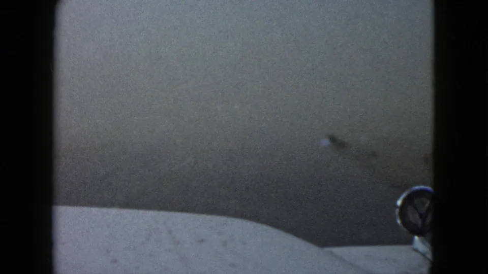 Fog begins to thin in this 1958 Las Vegas driving view, revealing the car hood edge and a round foreground emblem.