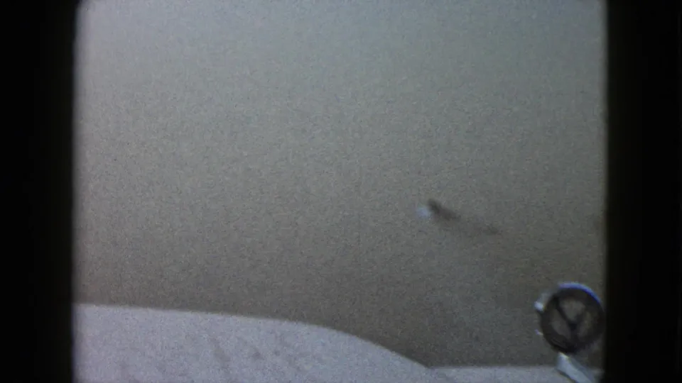 1958 8mm home-movie frame showing a close, soft view inside or beside a vehicle, with dark gate edge and a small round fixture visible.