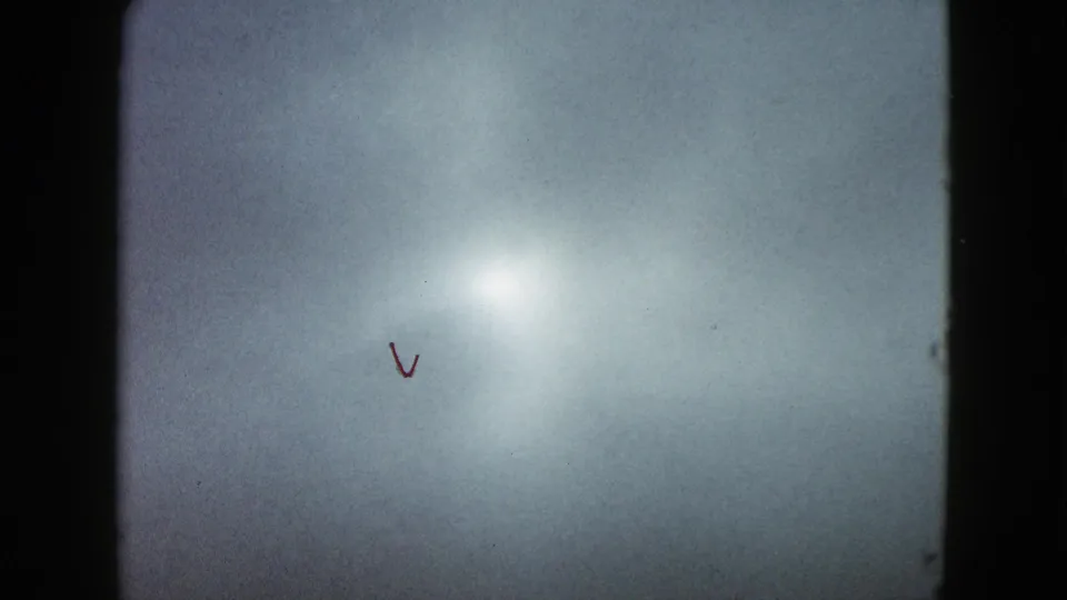 1958 8mm travel frame dominated by a bright exposure flare against a blue-gray surface, with small film or scene marks visible.