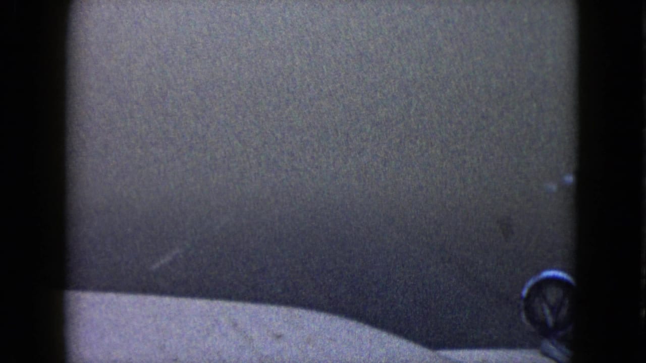 1958 Las Vegas home-movie frame showing a dim, grainy driving view with a pale vehicle edge and dark framing bars.