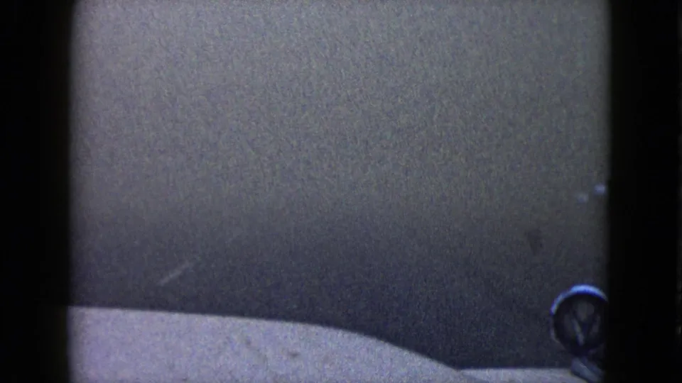 1958 Las Vegas home-movie frame showing a dim, grainy driving view with a pale vehicle edge and dark framing bars.
