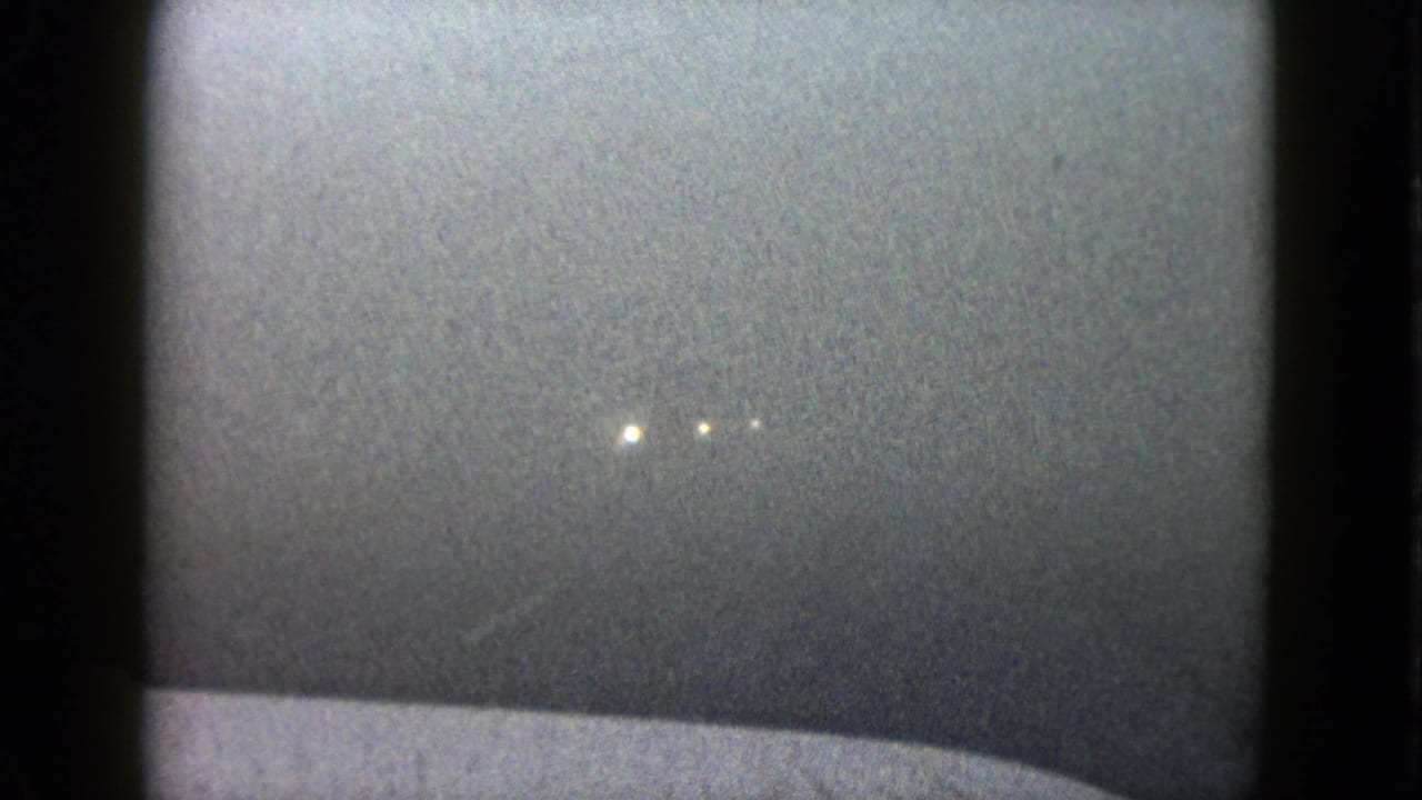 1958 Las Vegas frame with faint headlights emerging through haze above a pale vehicle hood or dashboard edge.