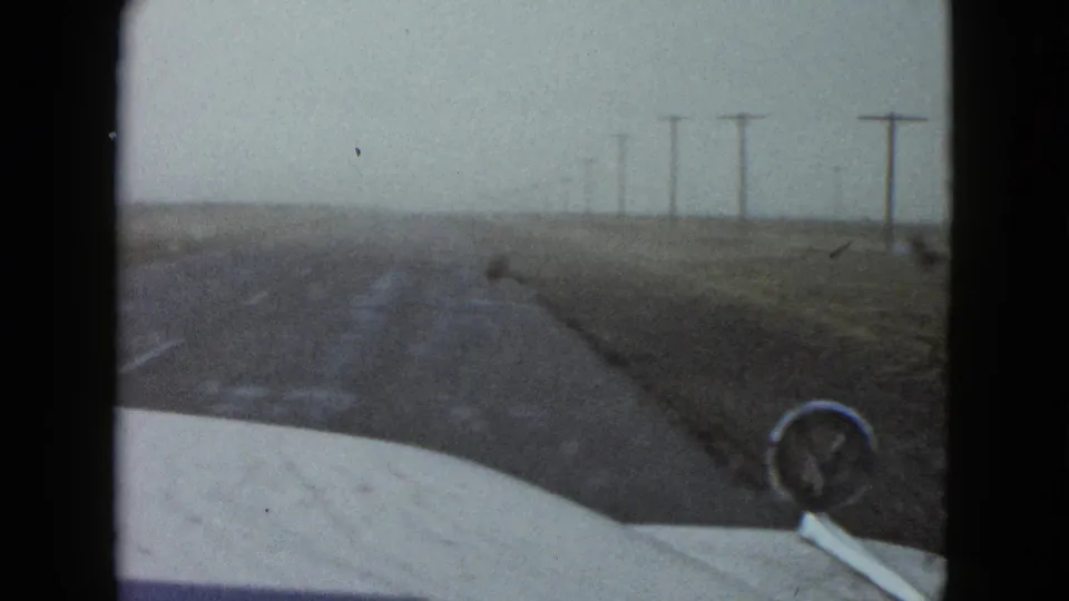 1958 Nevada travel footage looking over the car hood toward a rural roadway and a line of utility poles.