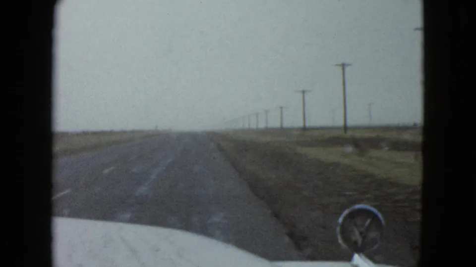 Windshield view on a 1958 Nevada road near Las Vegas, showing the car hood, straight roadway, and poles fading into the distance.