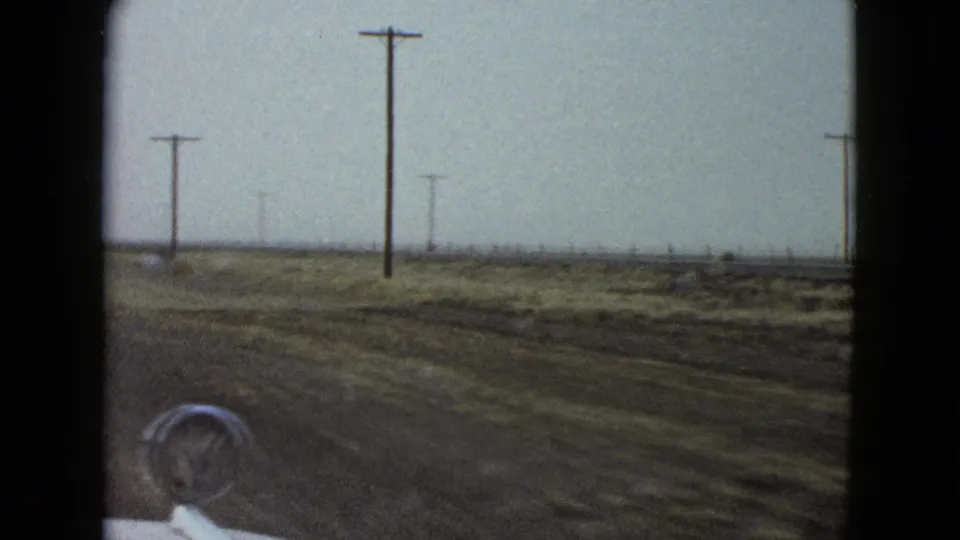A 1958 car-window perspective near Las Vegas shows a flat roadside landscape, wooden utility poles, and the car hood in the foreground.