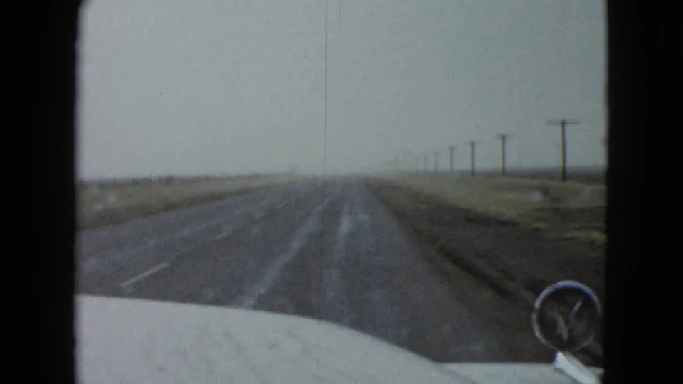 The 1958 Las Vegas travel clip ends on a forward view down a rural road, framed by a car hood, pole line, and flat open land.