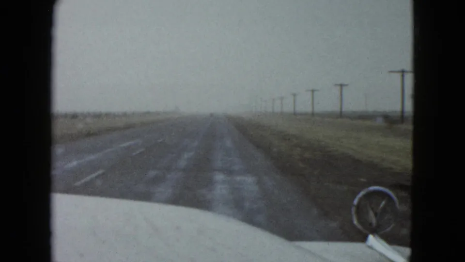 1958 Las Vegas-area home-movie view from inside a moving car on a straight rural road with utility poles receding ahead.