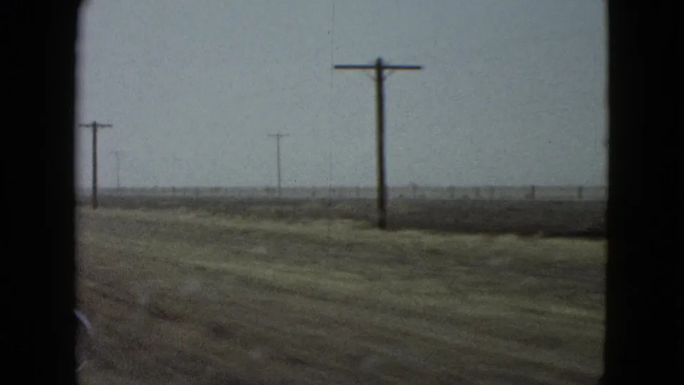 Rural Las Vegas roadside in 1958, viewed from a moving car past utility poles, dry grass, and flat open land.