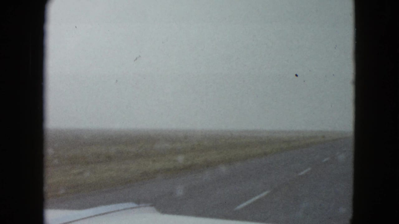 1958 8mm windshield view near Las Vegas showing a highway through flat open land with the car hood at the bottom edge.