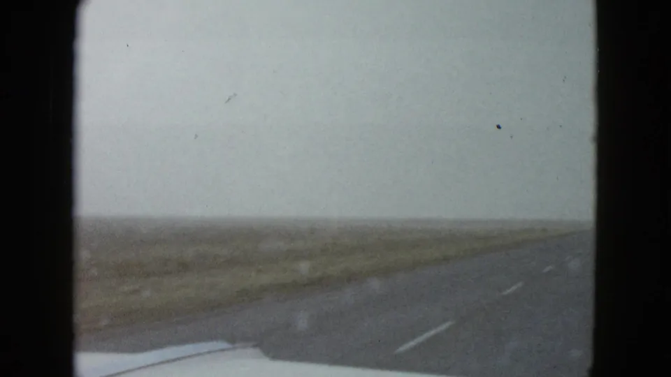 1958 8mm windshield view near Las Vegas showing a highway through flat open land with the car hood at the bottom edge.