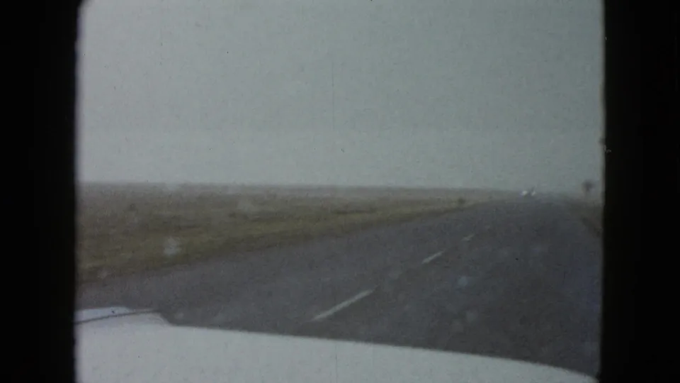 1958 8mm car POV near Las Vegas looking down an open highway bordered by low vegetation and distant utility poles.