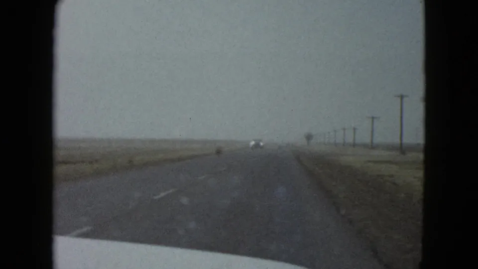 1958 8mm highway view near Las Vegas with a distant vehicle, roadside utility poles, and open plains under gray light.