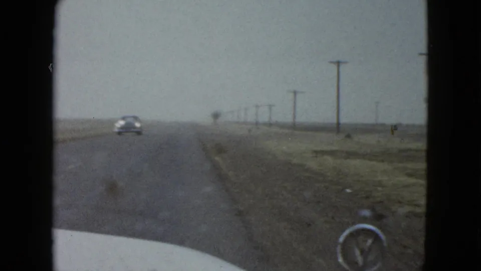 1958 8mm road-trip frame near Las Vegas showing a car ahead on a straight highway with utility poles and open land.
