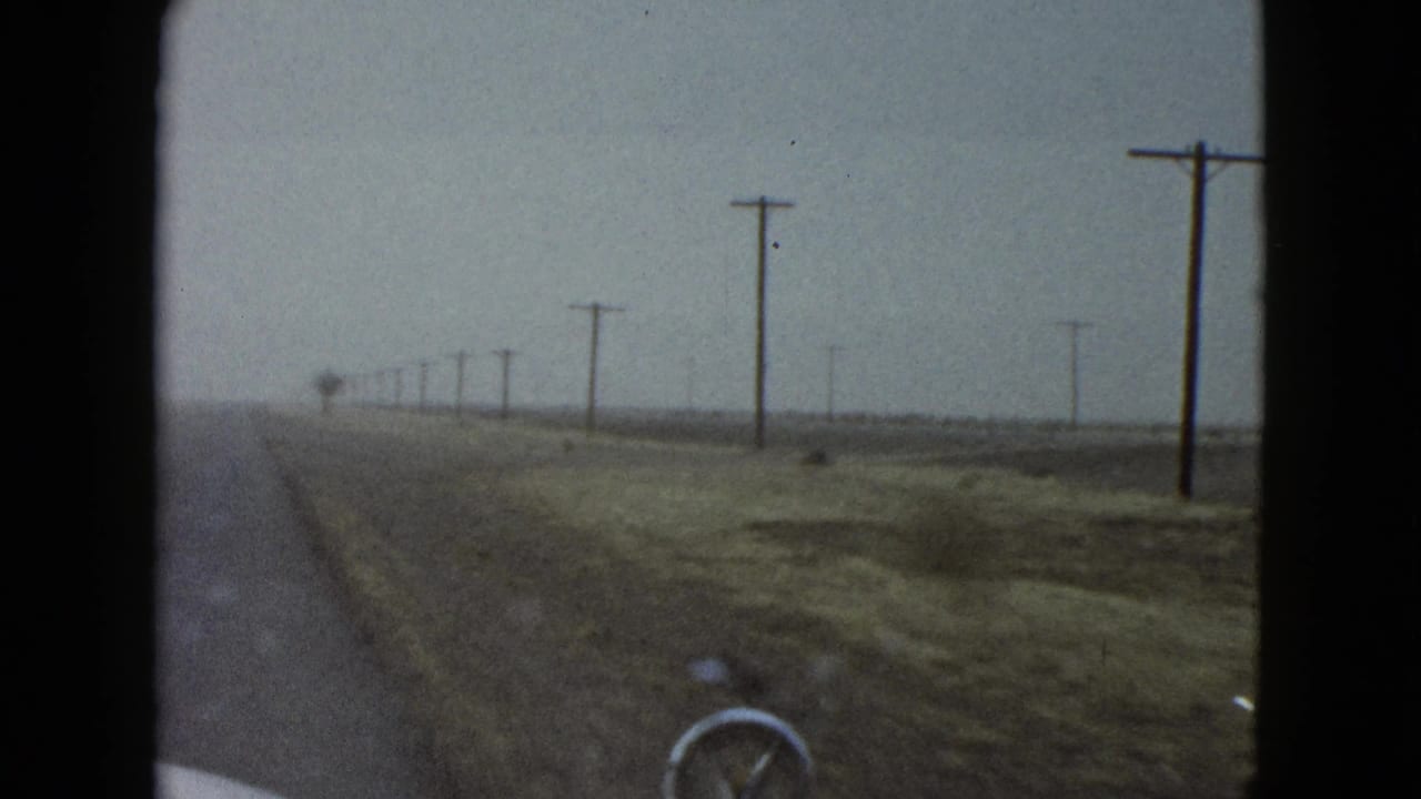 1958 Las Vegas-area home-movie frame from inside a car, showing a straight roadside landscape with utility poles and a pale hood edge.