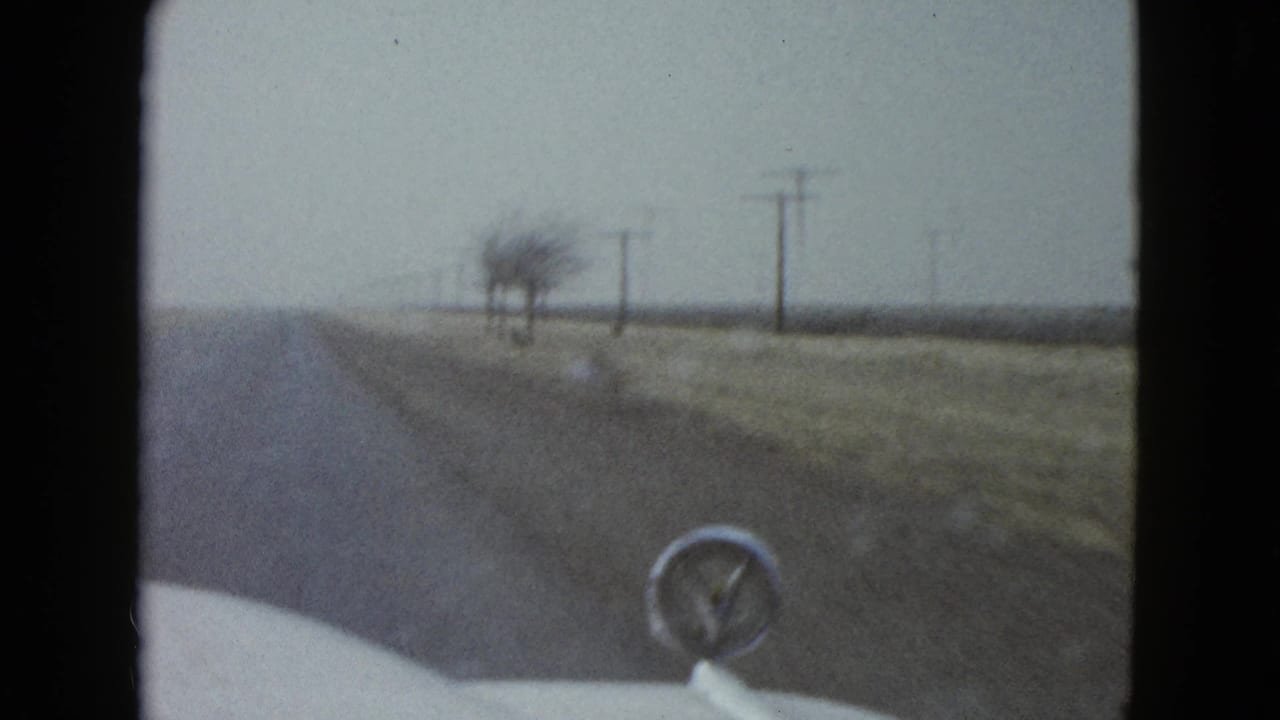 Forward view from a car on a rural road with utility poles and a hood ornament visible.