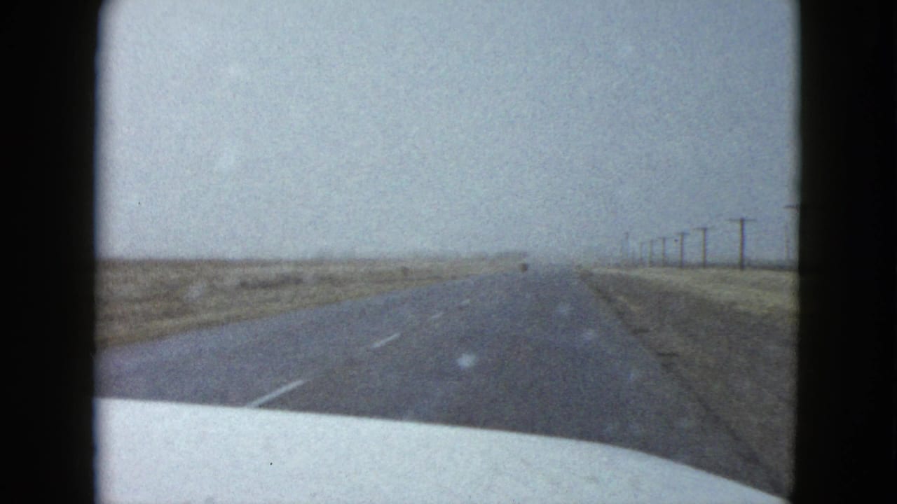 Driver’s-view 8mm frame of a wet Nevada highway receding into mist, with the white car hood at the lower edge.