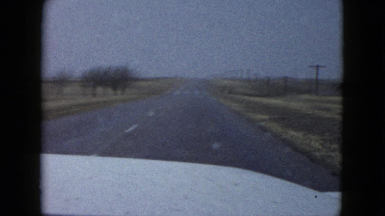 Two-lane rural road seen over a car hood under an overcast sky.