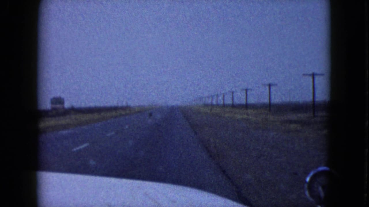 Windshield view of a straight desert highway with utility poles and car hood visible.