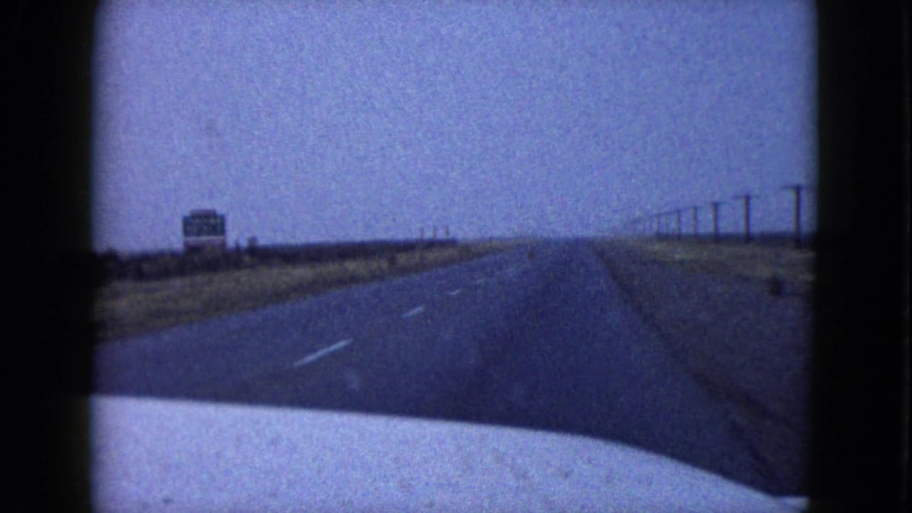 Desert highway seen through a car windshield with utility poles and a distant sign.