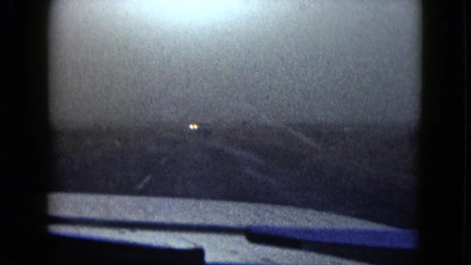 1958 8mm home-movie frame from near Las Vegas showing a dim car-window view of desert road with distant headlights.