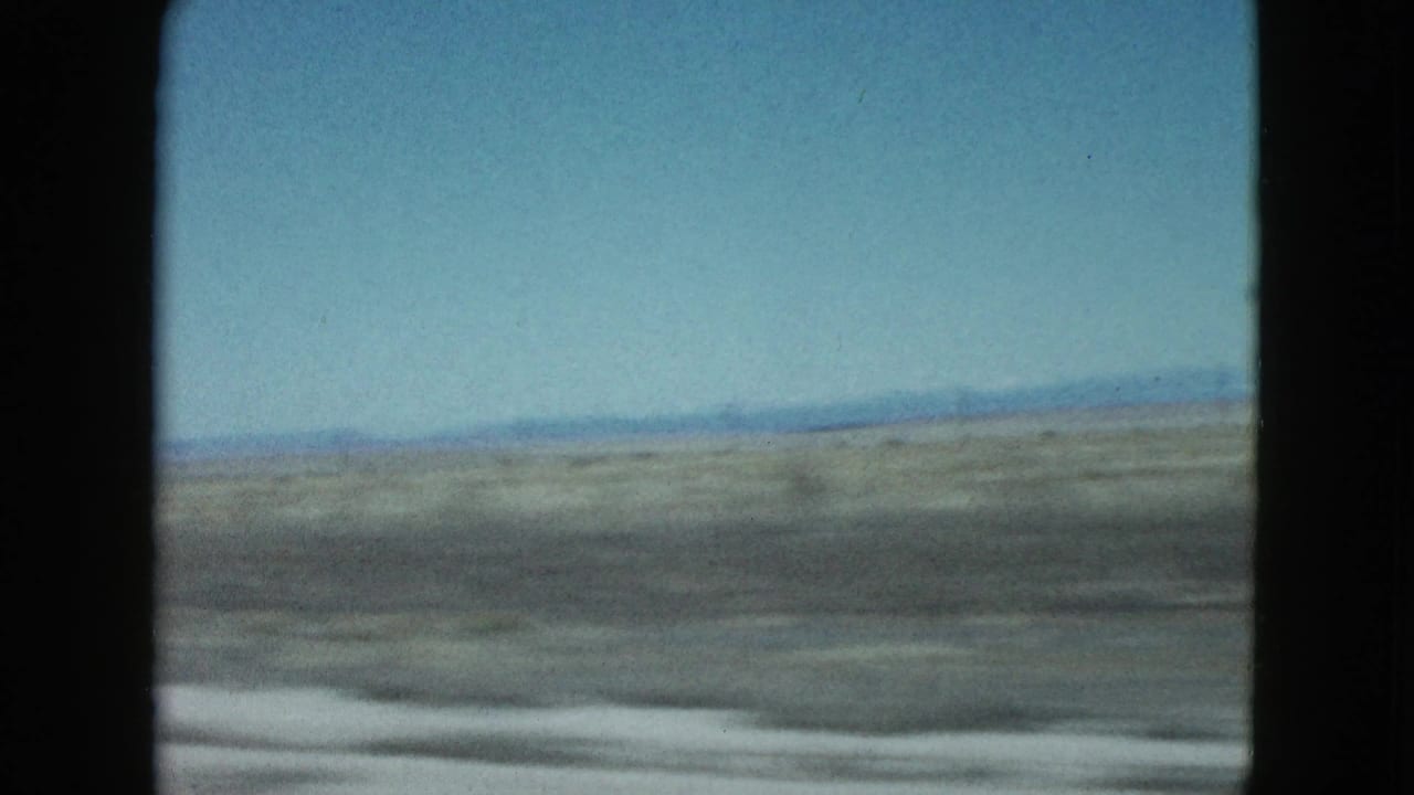 Blurred desert plain and blue sky seen from a moving vehicle.
